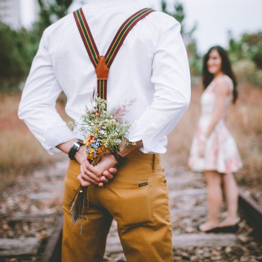 Un homme de dos cachant un bouquet de fleur à une femme